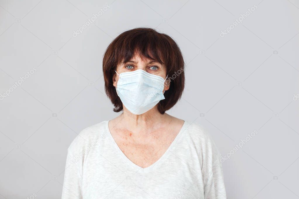 Mature woman in medical mask isolated on gray background