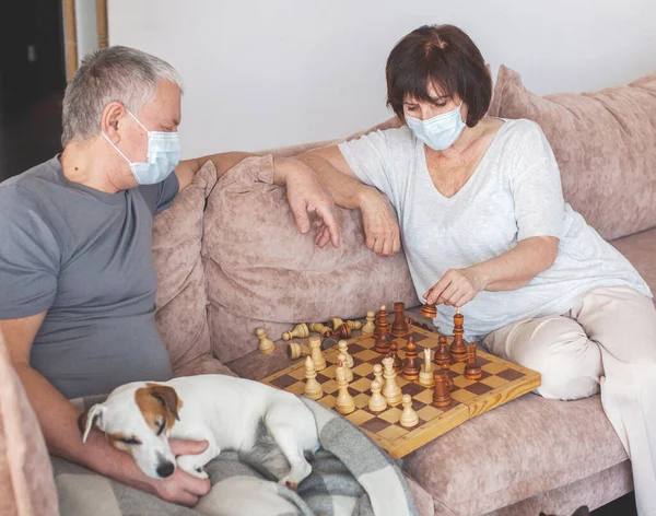 Idős pár orvosi maszkban a pandémiás koronavírus idején sakkozik. — Stock Fotó