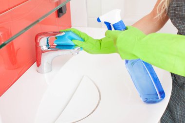 Kadın lavabo ve musluğu temizliyor.