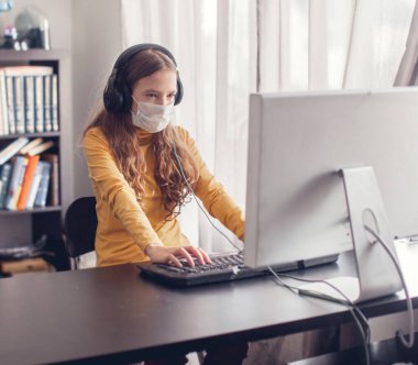 Evde bilgisayar başında, koruyucu maske takan genç oyuncular.