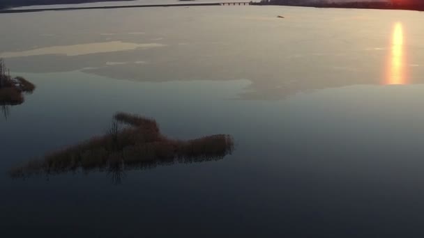 Vlucht over grote bevroren meer met bridge in de winter op zonsondergang, aerial view. — Stockvideo