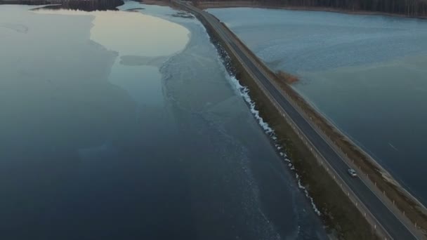 Vuelo sobre la carretera en el lago congelado al atardecer, vista aérea de invierno . — Vídeos de Stock