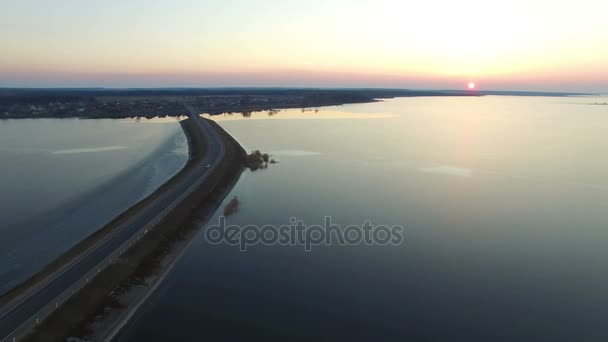 4K. Vuelo sobre la carretera en el agua helada en invierno al atardecer, vista aérea . — Vídeos de Stock