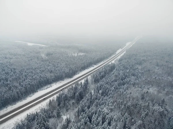 Straße im gefrorenen Winterwald mit fahrenden Autos. neblige Fluchtpunktperspektive. Luftpanoramablick auf den Norden. Stockfoto