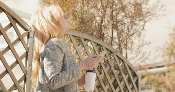 Schöne Frau schreibt Masseure auf das Handy, Mädchen trinkt Kaffee und lächelt — Stockvideo
