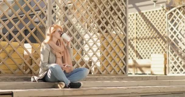Mädchen sitzt auf der Straße, trinkt Kaffee und schreibt eine Nachricht — Stockvideo