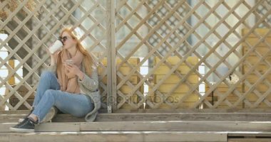 Güzel kadın merdivenlerde oturur, kahve içer ve bir ileti yazar