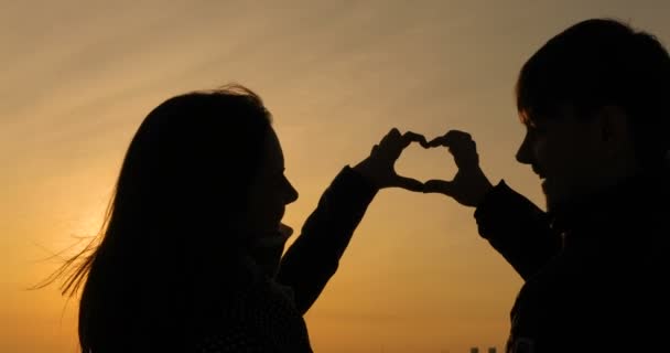Sol en las manos. Belleza chica y su novio haciendo forma de corazón por sus manos contra hermosa puesta de sol en el horizonte . — Vídeo de stock