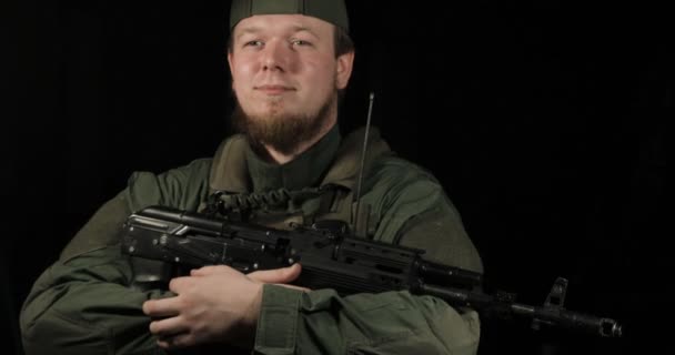 Солдат улыбается, держит АК-47, черный фон, крупный план — стоковое видео
