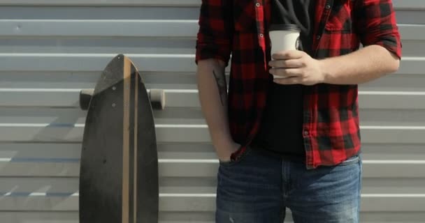 Junger Mann bleibt mit Longboard und trinkt Kaffee — Stockvideo