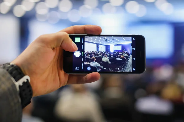 Público en una conferencia de negocios. Persona tomando fotos con un teléfono inteligente . — Foto de Stock