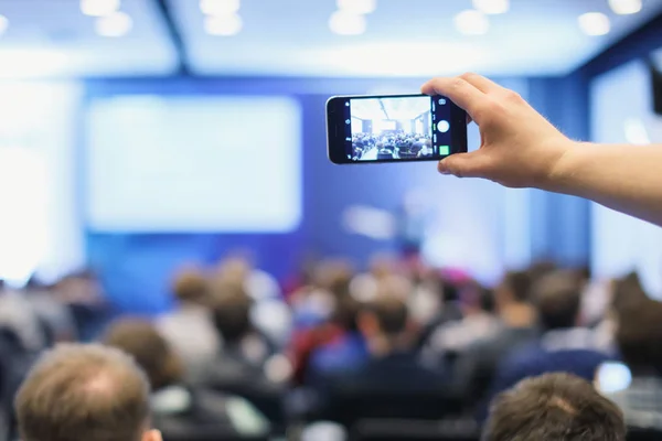 Audiência numa conferência de negócios. Pessoa tirando foto com telefone inteligente . — Fotografia de Stock