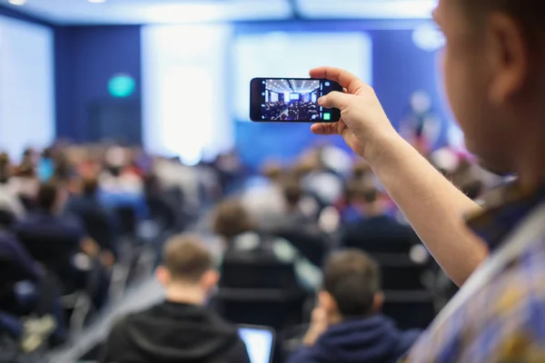 Audiência numa conferência de negócios. Pessoa tirando foto com telefone inteligente . — Fotografia de Stock