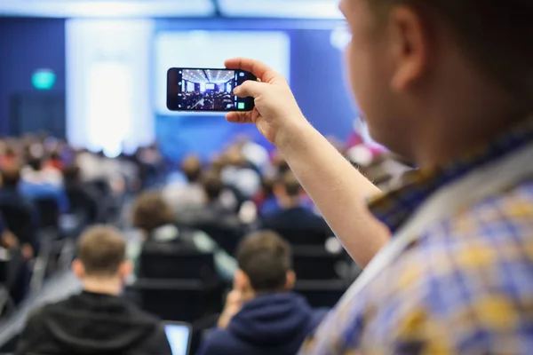 Público en una conferencia de negocios. Persona tomando fotos con un teléfono inteligente . — Foto de Stock