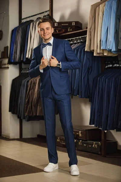 Homme d'affaires en gilet classique contre rangée de costumes dans le magasin. Un jeune homme élégant dans une veste en tissu noir. Il est dans la salle d'exposition, essayant des vêtements, posant. Photo publicitaire — Photo