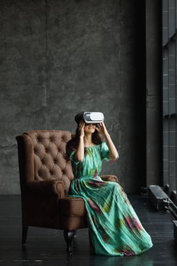 Yeni bir gerçeklik burada yakışıklı genç kadın Vr kulaklık, Vr kulaklık tasarım geneldir ve Hayır logoları, sanal gerçeklik, gözlüklü kadın oturur bir sandalye, karanlık bir arka plan.