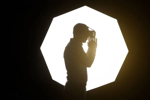 El diseño de auriculares VR es genérico y sin logotipos, Hombre con gafas de realidad virtual viendo películas o jugando a videojuegos. De pie cerca de la ventana, vista lateral, fondo, efecto bengalas — Foto de Stock