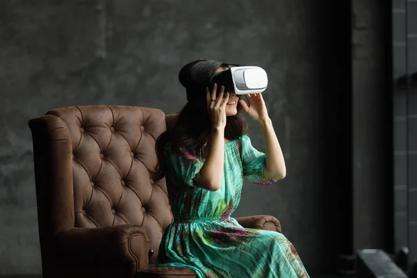 Yeni bir gerçeklik burada yakışıklı genç kadın Vr kulaklık, Vr kulaklık tasarım geneldir ve Hayır logoları, sanal gerçeklik, gözlüklü kadın oturur bir sandalye, karanlık bir arka plan.