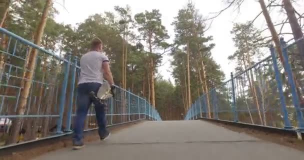 公園を歩いて彼のロングボードを持つ男。トラッキング ショット — ストック動画