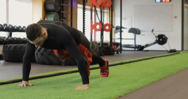 Un giovane in forma e fare flessioni in una piccola palestra, Sportsman esercizio in palestra. Muscoloso giovane che fa flessioni sul tappeto esercizio . — Video Stock