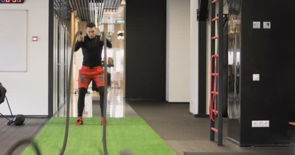 Молодой взрослый мужчина практикует упражнения на канате во время тренировки по кроссфиту в спортзале — стоковое видео