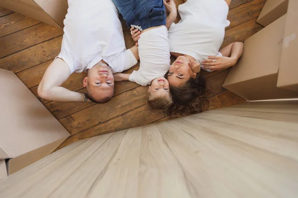 Vista dall'alto di un bel padre e madre giocare e abbracciare il loro piccolo figlio mentre sdraiato sul pavimento. famiglia che si rilassa e ride dopo aver disfatto i cartoni dal trasloco, Vista dall'alto — Foto Stock