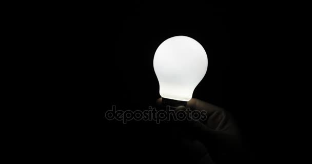 Hand holding a light bulb in the dark, the lamp lights up. black background, lamp concept — Stock Video