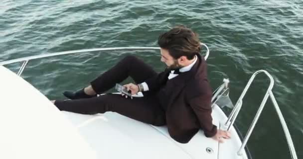Jovem empresário confiante usando telefone celular em um iate ou barco contra um mar. Viagens de luxo e trabalho . — Vídeo de Stock