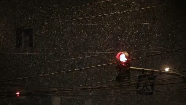 Stoplicht schijnt tijdens sneeuwval. Slecht weer, regen en natte sneeuw op de weg. reflecties nachtverlichting. Koplampen van de auto — Stockvideo