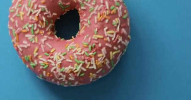 Brilhante e colorido donut polvilhado close-up macro tiro girando em um fundo azul. Delicioso donut doce girando em um prato. Vista superior — Vídeo de Stock