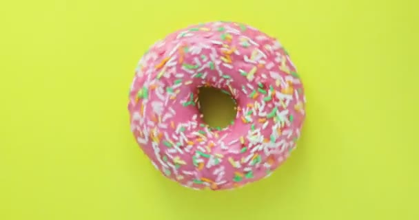 Brillante y colorido espolvoreado donut primer plano macro disparo girando sobre un fondo amarillo. Deliciosa rosquilla dulce girando en un plato. Vista superior — Vídeos de Stock