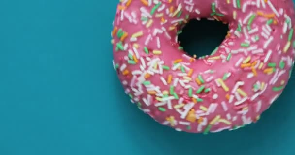 Delicious sweet donut rotating on a plate. Top view. Bright and colorful sprinkled donut close-up macro shot spinning on a blue background. Delicious sweet donut rotating on a plate. Top view — Stock Video