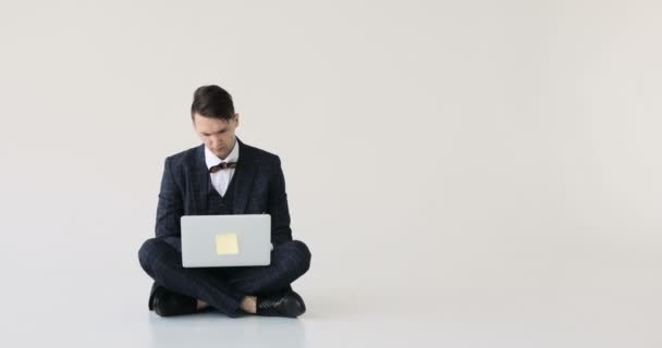 Stijlvolle zakenman in een pak zenuwachtig te typen op een laptop op een witte achtergrond — Stockvideo
