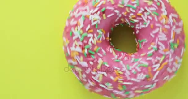 Hell und bunt bestreut Donut Nahaufnahme Makroaufnahme Drehen auf einem gelben Hintergrund. köstliche süße Donut rotierenden auf einem Teller. Ansicht von oben — Stockvideo