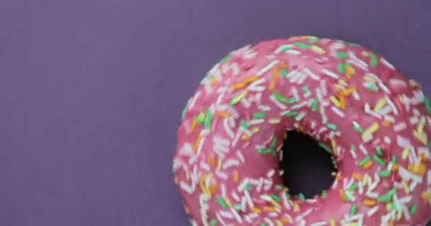 绚丽多彩的洒甜甜圈特写的微距拍摄上紫色背景旋转。美味甜甜甜圈在一个盘子上旋转。顶视图 — 图库视频影像