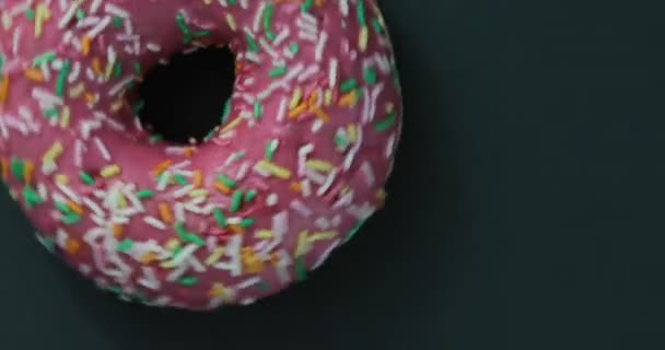 Lumineux et coloré saupoudré donut gros plan macro tournage sur un fond noir. Délicieux donut sucré tournant sur une assiette. Vue du dessus — Video