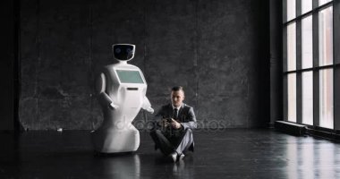 işadamı bir smartphone bir robot yanındaki yerde otururken kullanır. Modern robotik teknolojiler. Özerk insansı robot.