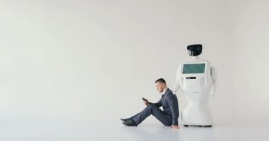 işadamı bir smartphone bir robot yanındaki yerde otururken kullanır. Modern robotik teknolojiler. Özerk insansı robot. Beyaz arka plan