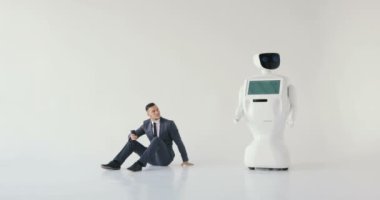 işadamı bir smartphone bir robot yanındaki yerde otururken kullanır. Modern robotik teknolojiler. Özerk insansı robot. Beyaz arka plan
