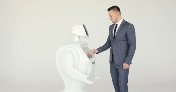 Un hombre elegante se comunica con un robot, presiona un brazo mecánico de plástico para el robot, apretón de manos. Sistema cibernético hoy. Tecnologías robóticas modernas. Robot autónomo humanoide. fondo blanco — Vídeos de Stock