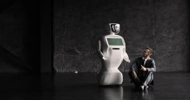 Affärsman använder en smartphone när du sitter på golvet bredvid en robot. Modern Robotic teknik. Humanoid autonom robot. — Stockvideo