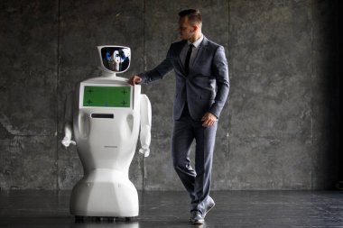 Şık bir adam bir robot ile iletişim kurar. Sibernetik sistem bugün. Modern robotik teknolojiler. Özerk insansı robot. çatı katı ofis