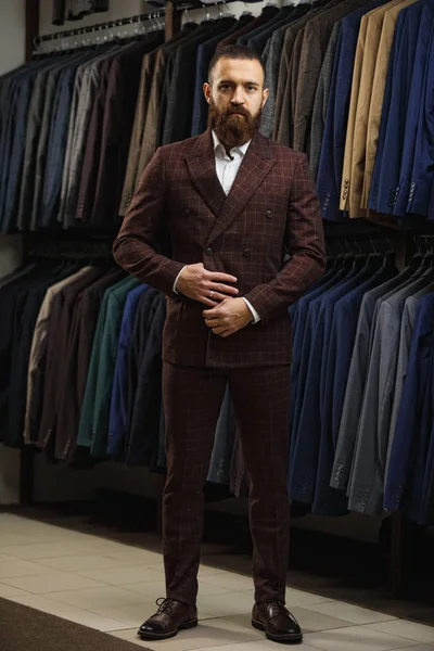 Sakallı adam kameraya ararken bir dükkan takım elbiseli ile raf yakınındaki elbiseli tam uzunlukta portresi
