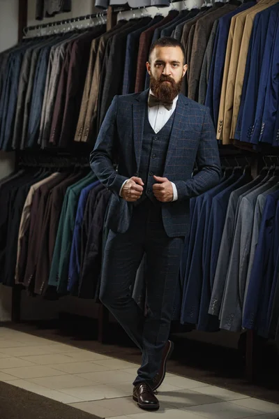 Sakallı adam kameraya ararken bir dükkan takım elbiseli ile raf yakınındaki elbiseli tam uzunlukta portresi