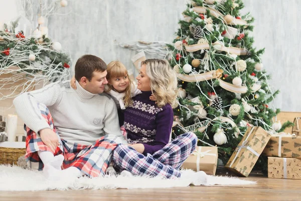 Una familia divertida y feliz con regalos de Navidad. Los padres y el pequeño bebé se divierten cerca del árbol de Navidad en la habitación. Familia cariñosa junto al árbol de Navidad — Foto de Stock