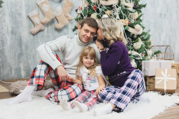 Una familia divertida y feliz con regalos de Navidad. Los padres y el pequeño bebé se divierten cerca del árbol de Navidad en la habitación. Familia cariñosa junto al árbol de Navidad — Foto de Stock