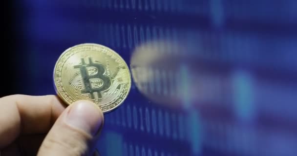 Homem detém bitcoin contra monitor com código binário — Vídeo de Stock