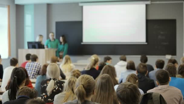 Oogpunt van achter een groep studenten in een klaslokaal, luisteren als hun leraar een lezing houdt. Achteraanzicht — Stockvideo