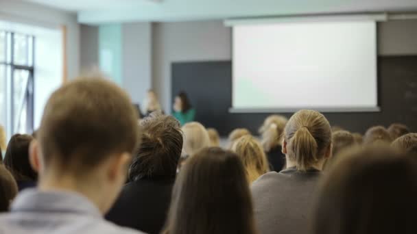 Vy bakifrån av en grupp elever i ett klassrum, lyssnar som deras lärare håller en föreläsning. bakifrån — Stockvideo