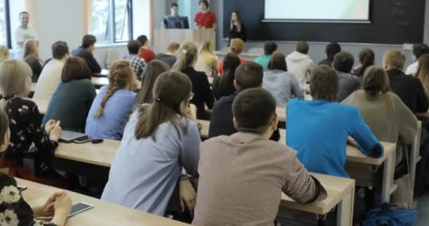 Grupo de estudiantes universitarios sentados en sus escritorios en el auditorio y escuchando mientras su profesor imparte una conferencia . — Vídeo de stock